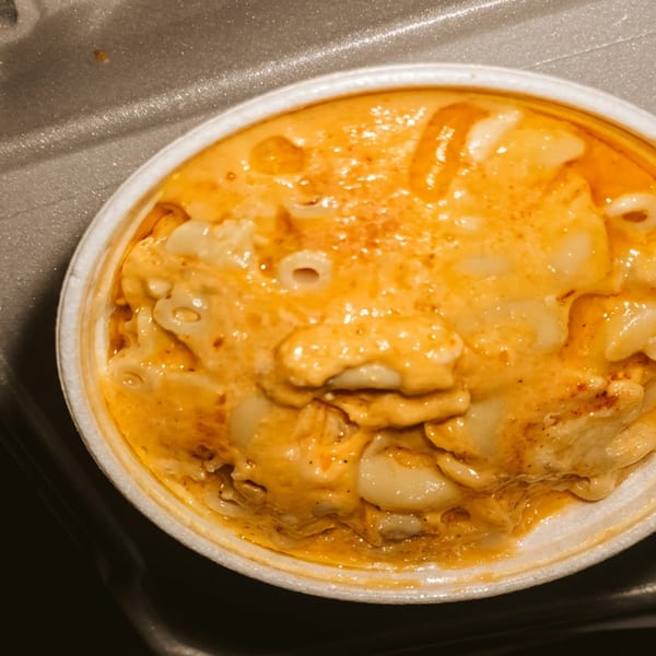 Creamy orange mac and cheese in a white bowl on a gray takeout container.