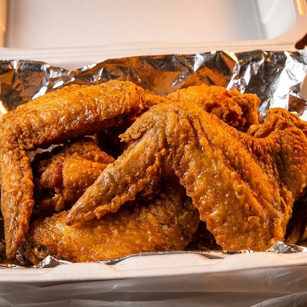 Crispy fried chicken wings in a foil-lined takeout container inside a plastic bag.
